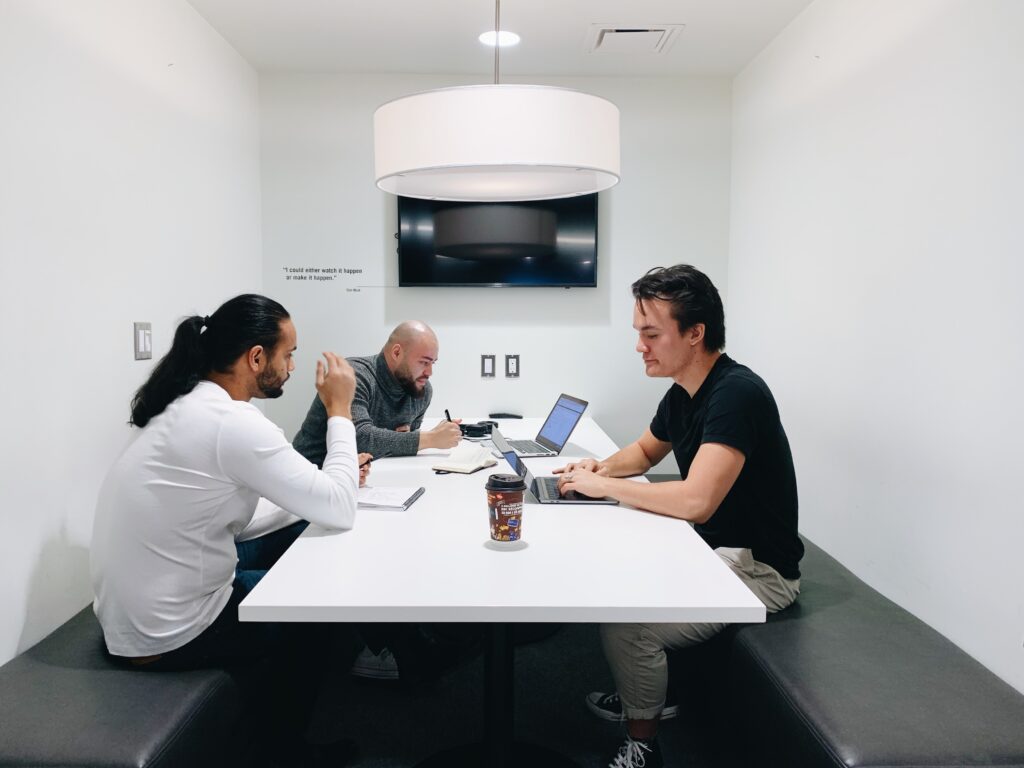 Team members talking in a meeting room, with coffee and laptops visible.