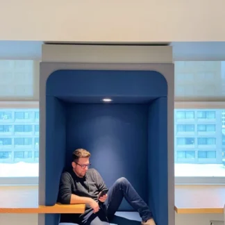 Member lounging in blue booth, with desks and windows visible.