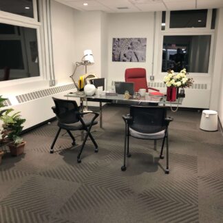 Private office with flowers and comfortable red chair, with multiple windows behind.